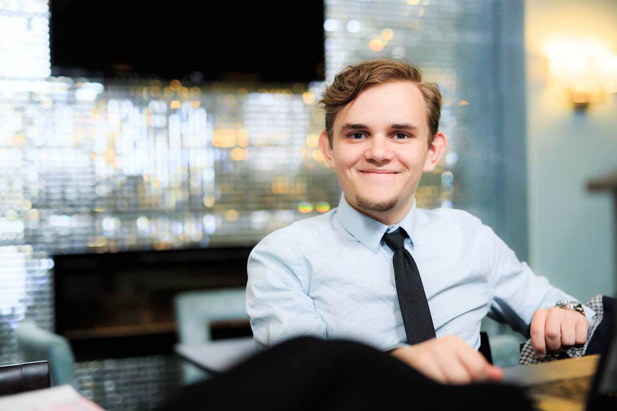 A young man in a shirt and tie sits at a work computer