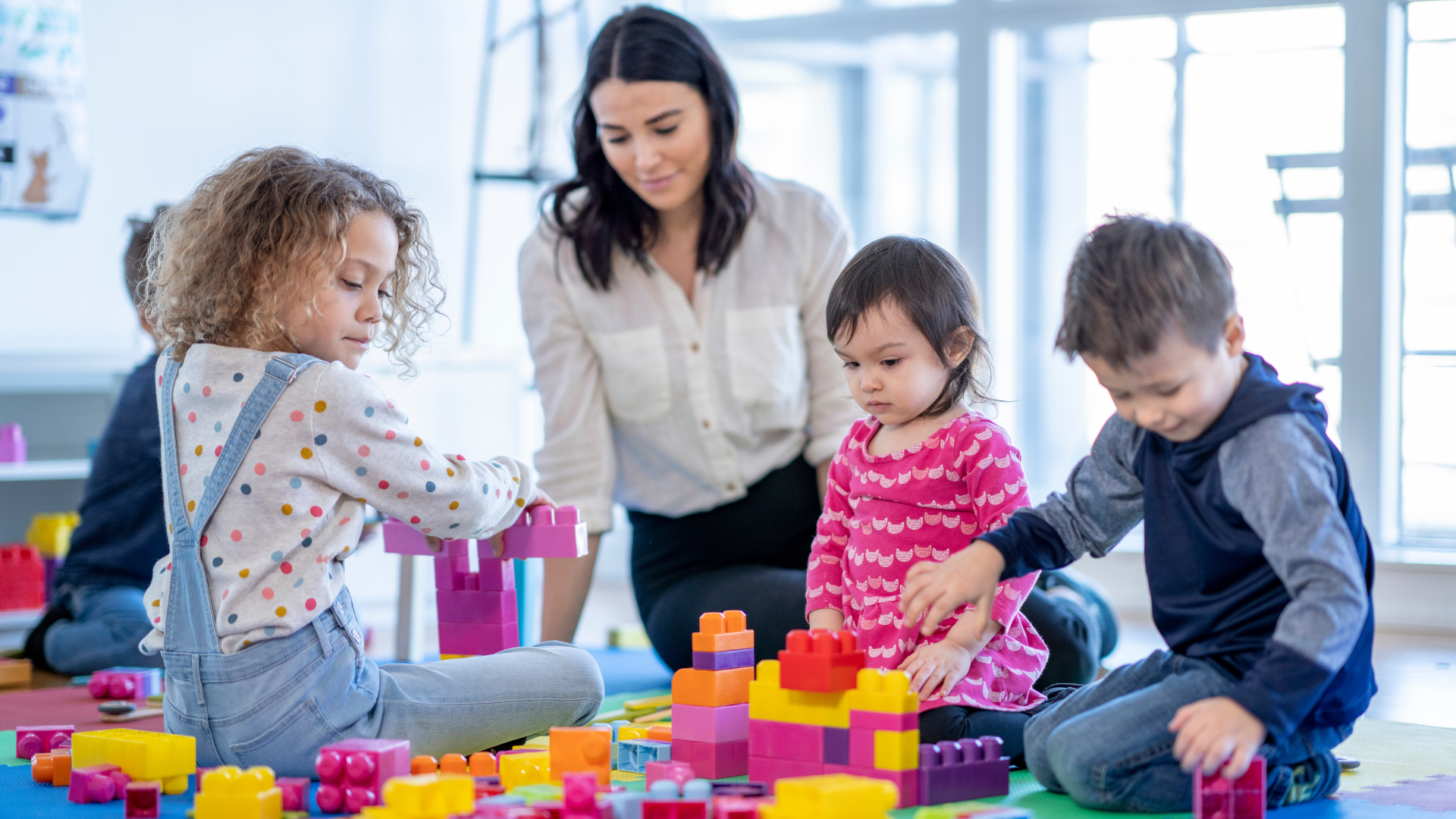 A child care worker watches over a group of young children playing with blocks