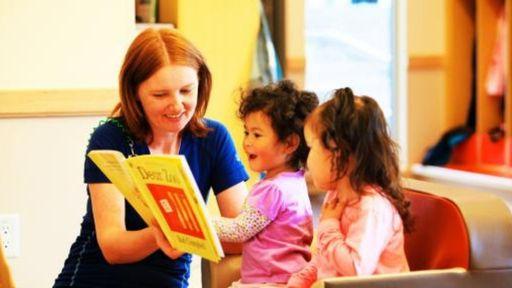 Two young girls read a book with a staff member at a YMCA child care location