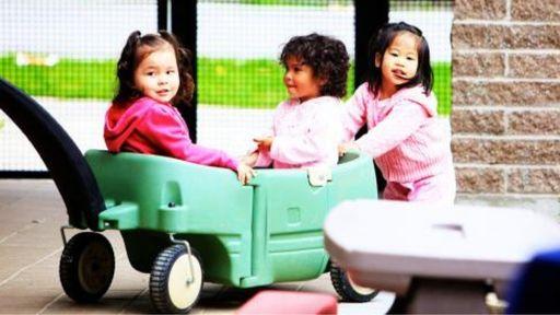 Three young girls play with a children's wagon outside