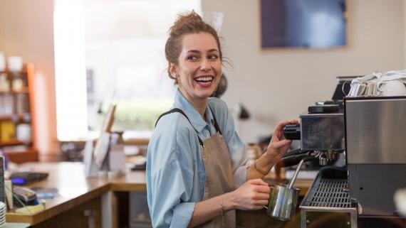 A smiling woman working as a barista makes a coffee.